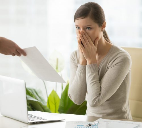 Young woman shocked when receiving dismissal notification from boss. Upset female employee worrying because of mistakes in calculations. Office worker can not believe in breaking employment contract